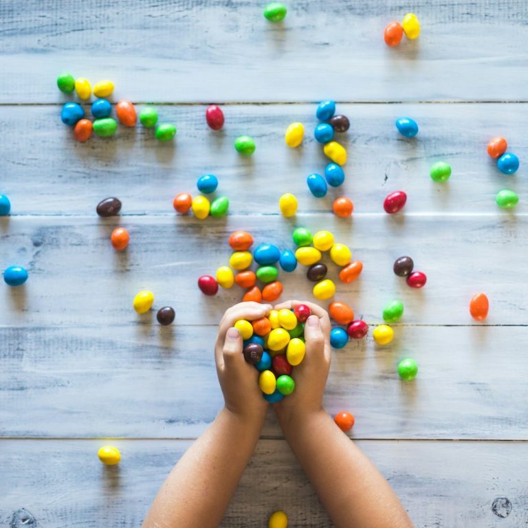 Hands and colourful candy Hands hold colourful candies, with more scattered on a wooden surface.